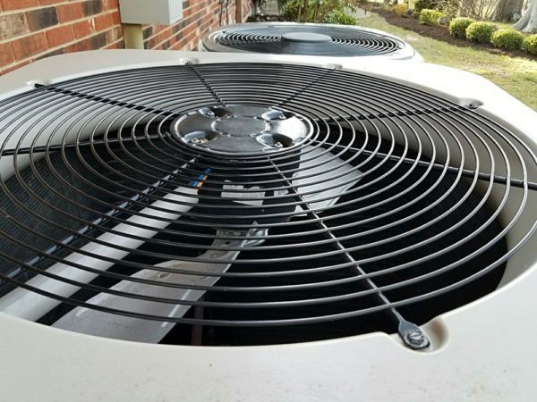 Close-up of an outdoor AC unit serviced by Jerry Kelly Heating and Air, highlighting its metal fan grille and another unit behind.
