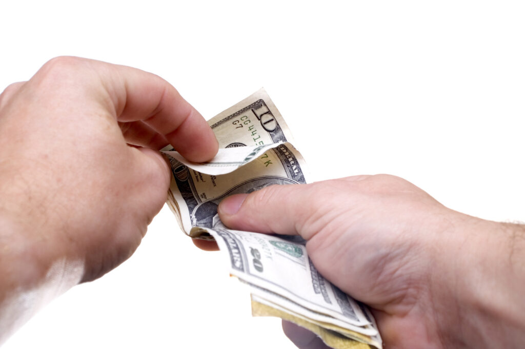 Two hands counting and holding a stack of U.S. dollar bills against a white background.