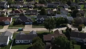 Aerial view of a suburban neighborhood with single-family homes, tree-lined streets, and a green van driving down the road.