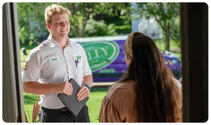 %Title% | Jerry Kelly Heating, Air Conditioning, Plumbing, &Amp; Electrical A service technician holding a tablet speaks with a customer at her door, with a branded company van parked outside in a residential neighborhood.