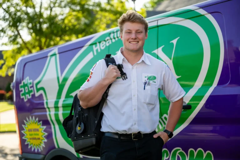 A technician in uniform stands in front of a colorful service van, holding a black bag and smiling at the camera.